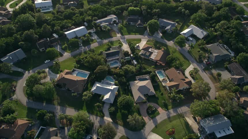 A birds eye 5K aerial view of a suburban cul-de-sac in Stuart Florida during a partly cloudy Florida sunset tilting down to show the single-family homes