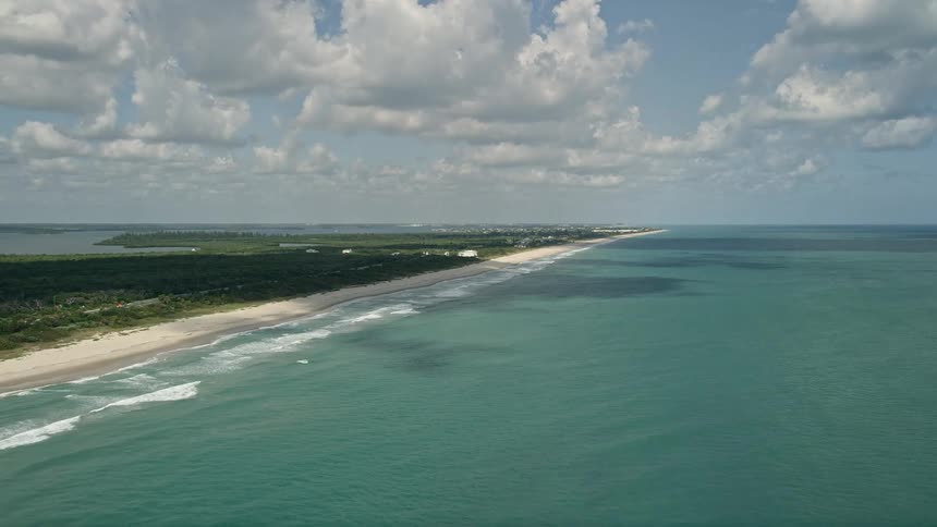 Approaching the beautiful empty beach and blue waters of Vero Beach Florida from an aerial during summer with partly cloudy skies