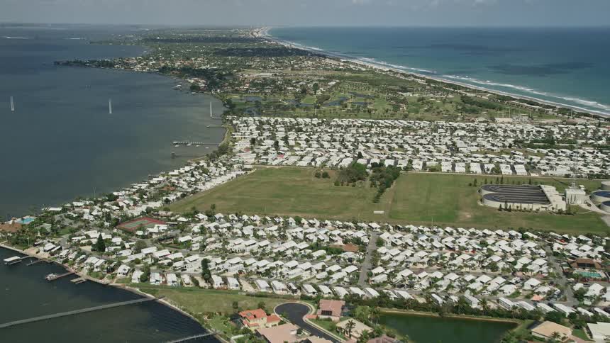 A daytime aerial footage tilt up from a riverside residential neighborhood revealing a mobile park surrounded by RV parks and waterfront properties in Melbourne Beach Florida