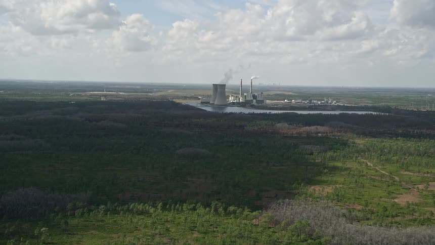 Aerial view approaching a coal-fired power generation facility with smoking chimneys in Orlando Florida on a partly cloudy day