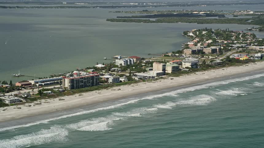 Aerial footage of a partly cloudy day at Cocoa Beach Florida showing beachfront condominiums along the shoreline and sunbathers enjoying leisure activities