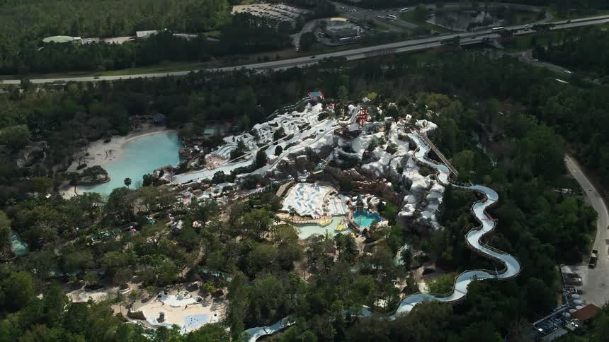 Aerial footage of Walt Disney Worlds Blizzard Beach water park in Florida on a partly cloudy day providing sightseeing and entertainment for visitors enjoying water slides and leisure activities in an amusement park surrounded by lush greenery