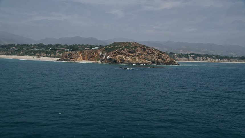 Approaching the rugged coastal cliffs of Point Dume in Malibu California from an aerial revealing the beautiful shoreline and blue ocean waters