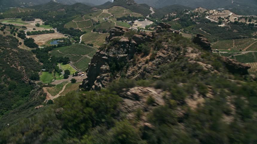 An awe-inspiring aerial view of vineyards nestled on the hills of Malibu California as the camera pans out to reveal a jagged slope