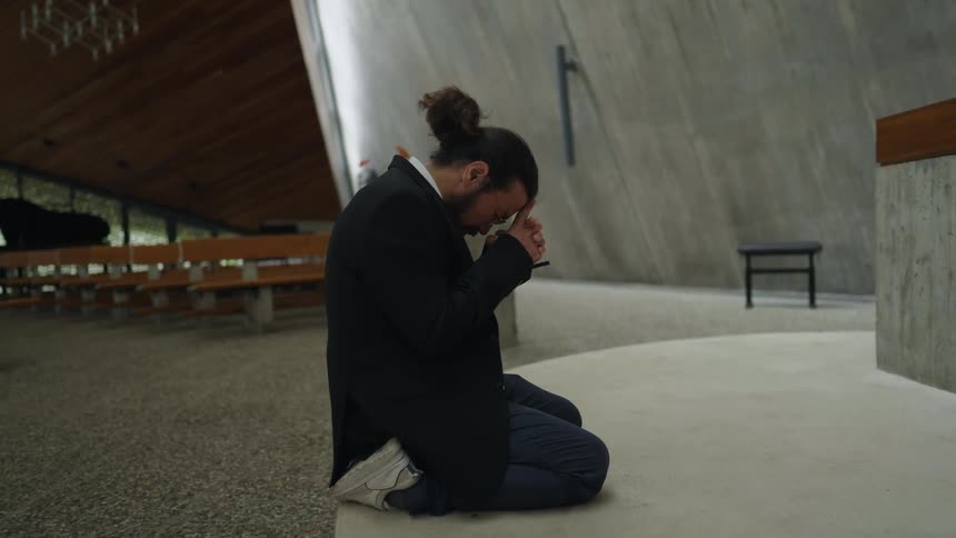 A young man in a temple or church positioned on his knees in an act of prayer