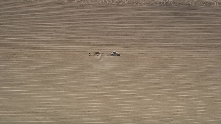 A tractor tills the soil of a sunny California farm field from an aerial perspective