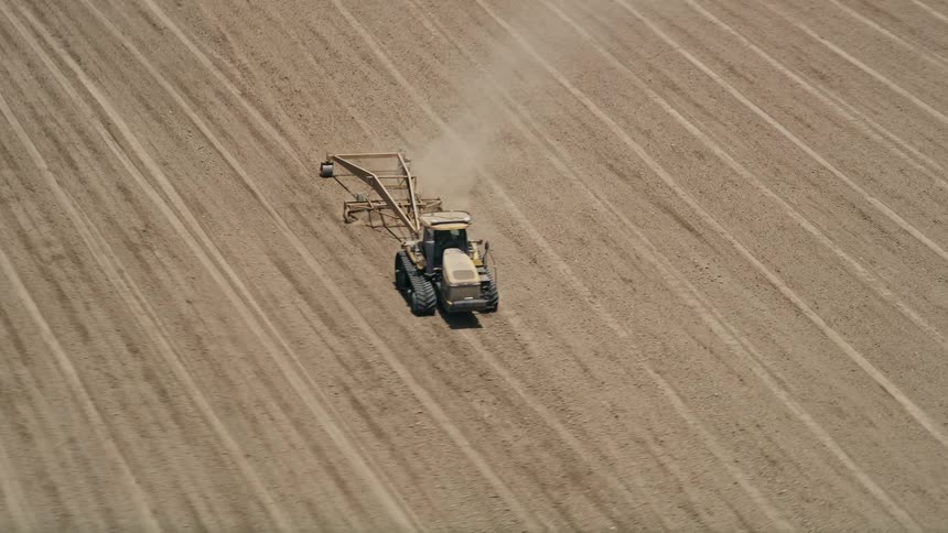 Aerial view of a tractor tilling a vast field in Camarillo California during a sunny day