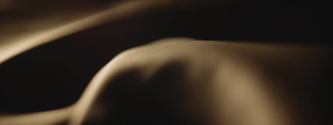Light shines on a tan surface with a smooth texture and curves with shadows in the folds