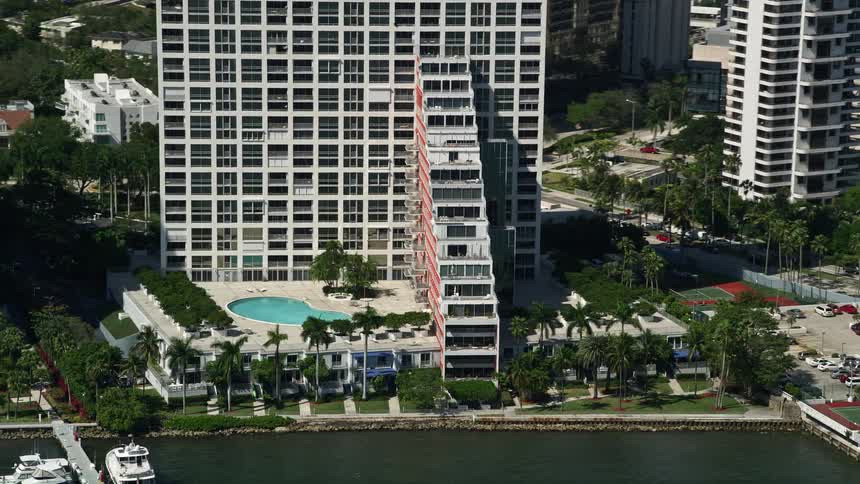 A stunning aerial view of an apartment building with a pool and boats on its pier situated on the shores of Biscayne Bay in Miami Florida