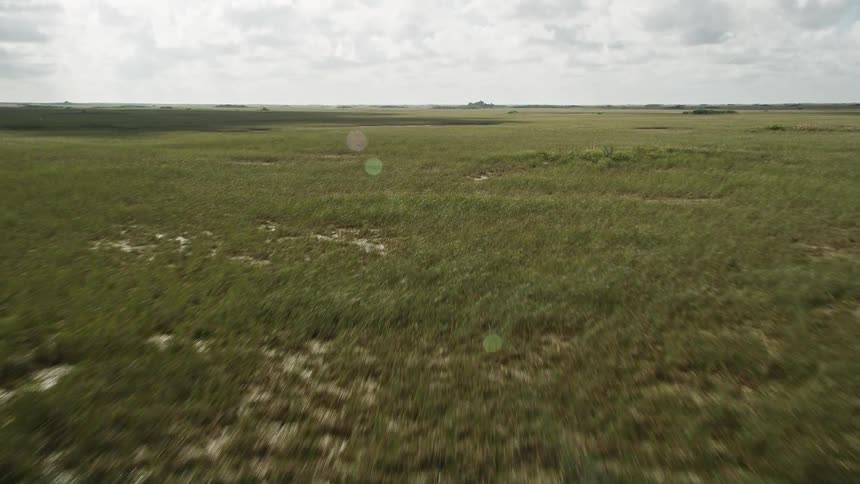 Flying over the marshland of Florida Everglades showcasing the natural landmark with partly cloudy skies and shadowy landscape captured in aerial footage