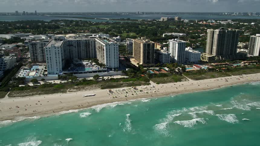 A beautiful aerial view of The Perry South Beach in Miami Florida with crystal blue water light waves and sunbathers enjoying the sunny day on the beach