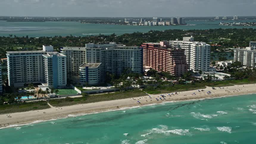 Aerial footage of The Alexander All Suite Oceanfront Resort in Miami Beach Florida showcasing condo buildings lining the waterfront behind a popular beach