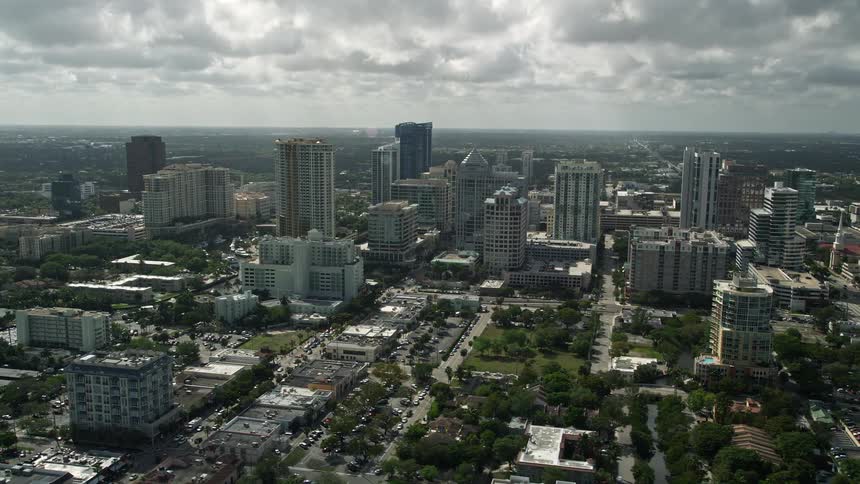 Aerial footage of downtown Fort Lauderdale Florida captured from a side view as the camera orbits around tall buildings and skyscrapers showcasing the citys river waterways and water bodies on a partly cloudy day