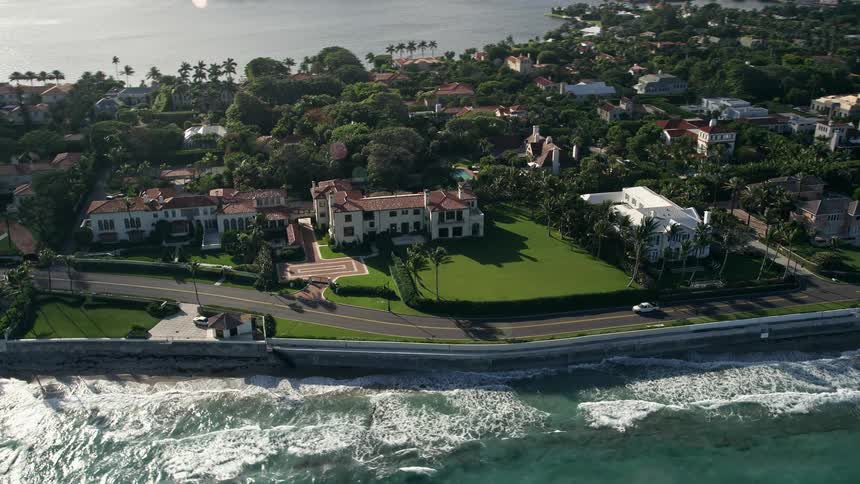 Flying over Palm Beach Floridas coastal mansions with partly cloudy skies and shoreline visible