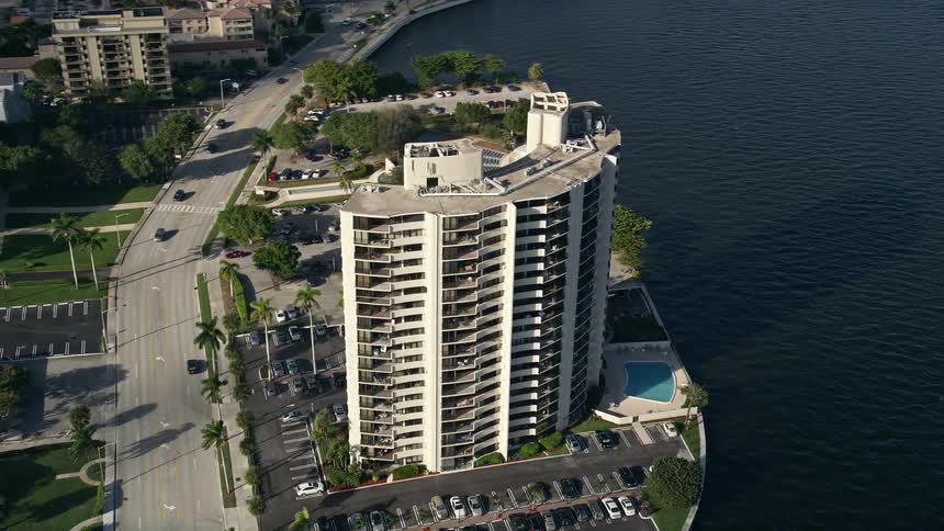 Aerial view of a tall apartment building orbiting around the Intracoastal Waterway and West Palm Beach in Florida with partly cloudy skies