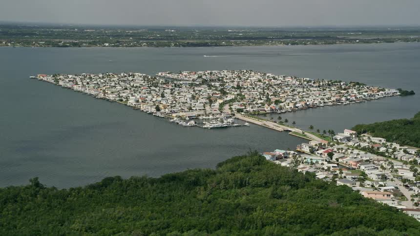Aerial footage of houses on the waterfront community of Nettles Island in Jensen Beach Florida with partly cloudy skies and a view of the surrounding residential area