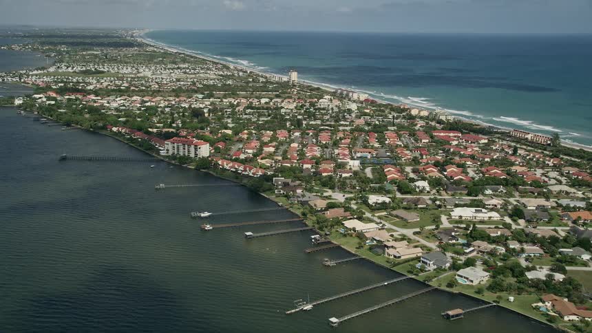 An aerial view of a residential neighborhood on the riverbank in Melbourne Beach Florida with apartment buildings and houses overlooking the shorelines and docks while tilting down from the sky