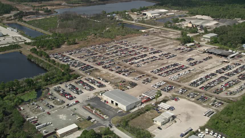 Approaching aerial view of an auto salvage lot with cars parked in a partly cloudy day in Cocoa Florida