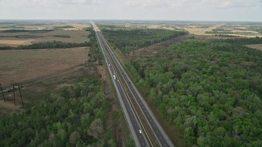 An aerial of a highway approaching the rural town of La Belle Florida surrounded by trees on either side and partly cloudy skies