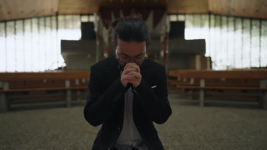 A man kneeling with his hands clasped in front him while he prays in a church foyer