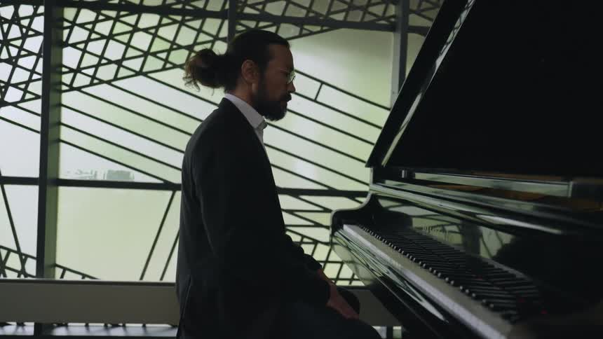 A man in a suit sits down at a grand piano