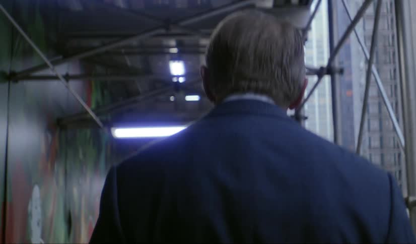 An old man in a business suit walks along a city street near a mural