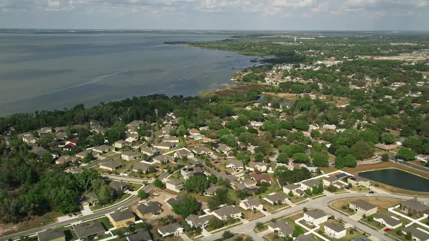 Fly over residential neighborhoods along a shoreline by a lake in Winter Garden Florida shot during daytime aerials with partly cloudy skies