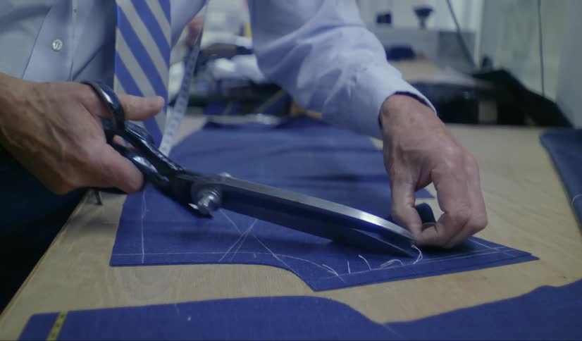 A close up of a mans hand using large scissors to cut extra thread on material