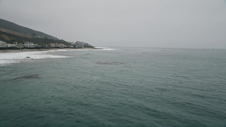 A low flying aerial view of Malibus coastal community with ocean kelp and oceanfront homes along the shoreline of the Pacific Ocean in Southern California