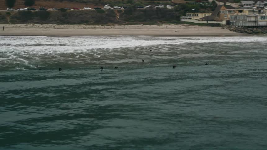 A group of surfers are seen catching waves in Malibu California as the camera tracks them from above
