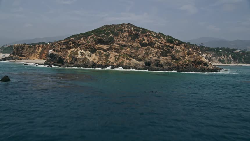 A mesmerizing aerial view of the Californian coast revealing the Point Dume and its rocky cliffs as the drone approaches