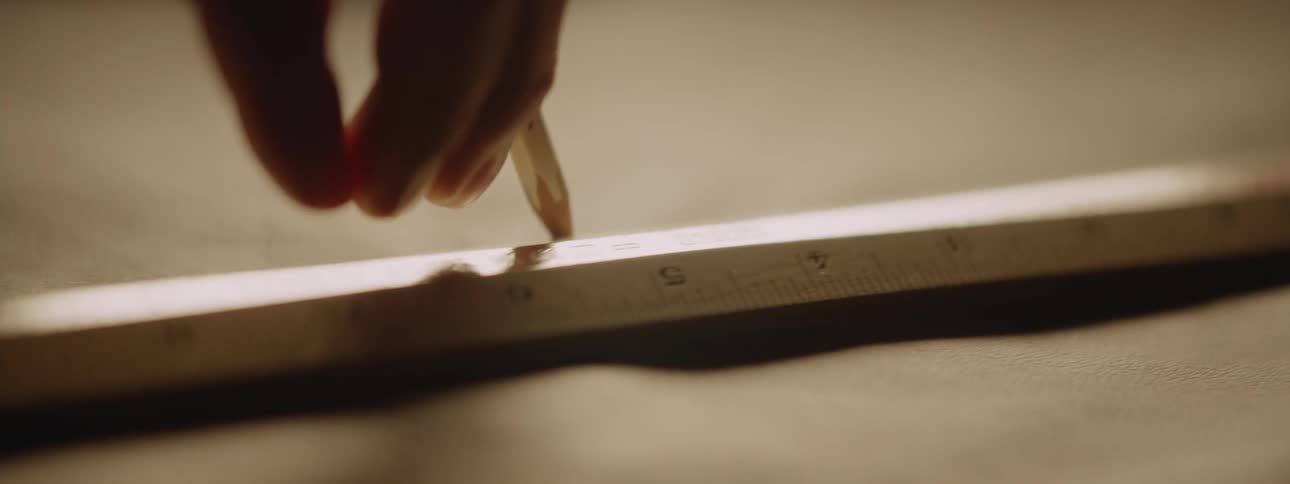 A hand draws a line on fabric with a pencil following a ruler