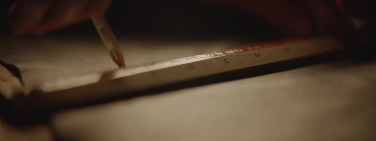 A close up of a person using a pencil to mark along a ruler on paper