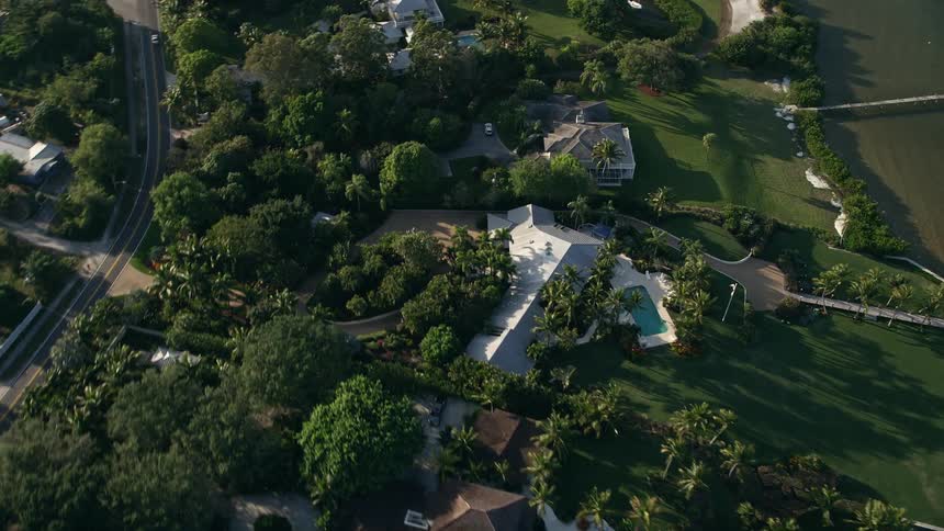 Flying over a treelined suburban neighborhood with luxurious homes and pools on the shore of Stuart Florida during dusk