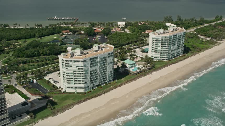 This is an aerial view of a condominium complex on Jensen Beach Floridas coast with partially cloudy skies and people enjoying the beach in the daytime