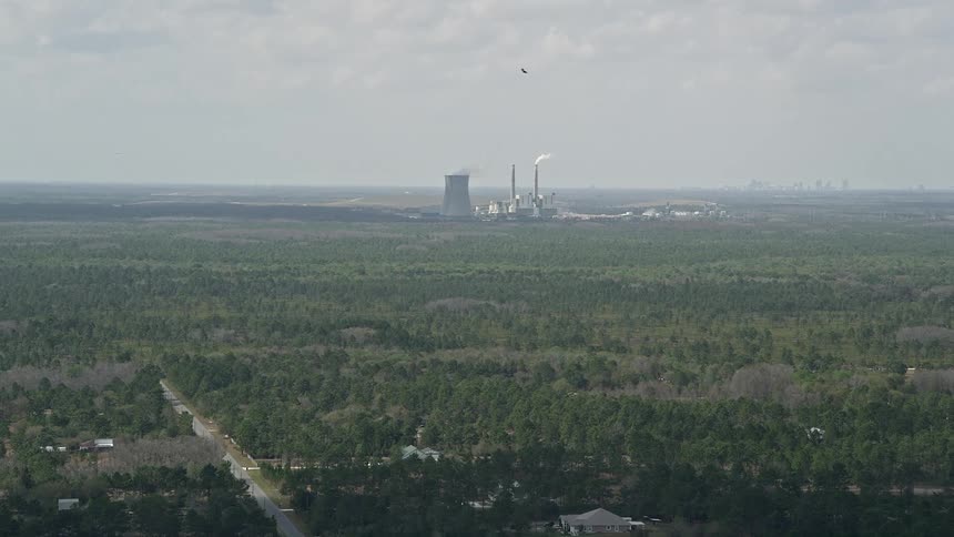 Flying over trees heading towards a coal-fired power plant in Orlando Florida on a partly cloudy day