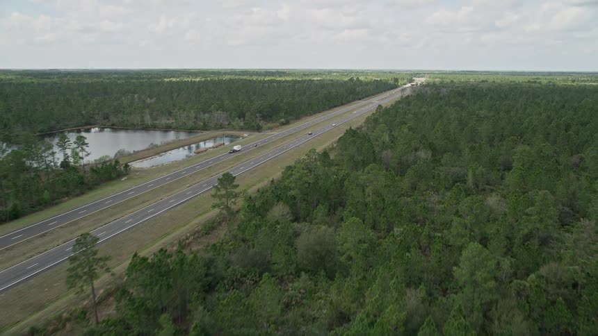 A stunning aerial view flying low over lush green forests and a highway in Cocoa Florida during summertime