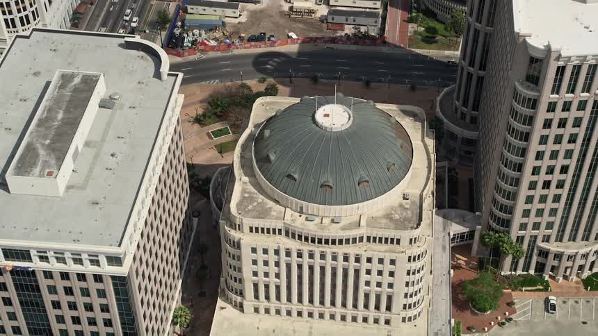Approaching and tilting down to a birds eye of Orlando City Hall in downtown Orlando Florida on a partly cloudy day