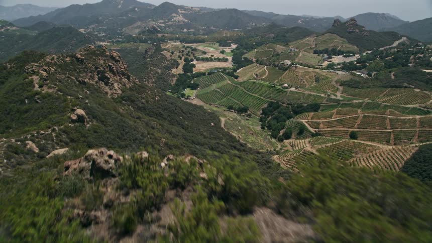 Approaching and flying over striking rock formations to reveal hilly vineyards under the warm California sunshine in Malibus rustic winery with stunning aerial views