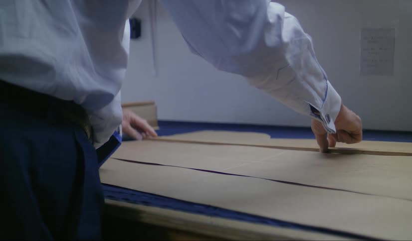 A man wearing a shirt and tie using a ruler on brown paper measuring and marking it off