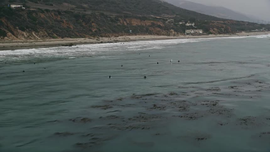 The aerial video flies low over the ocean passing surfers waiting for waves near Malibu California