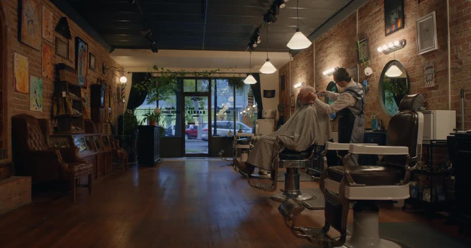 A barber trims the hair of a customer in a barber shop during the day