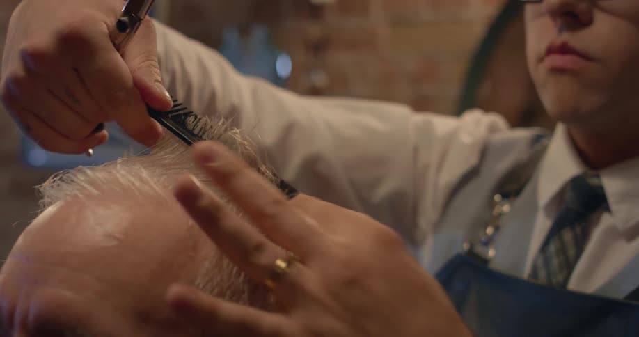 A barber trims the top of a mans hair