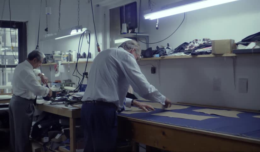 Two men cutting patterns from brown paper on an assembly table in a clothing design studio daytime