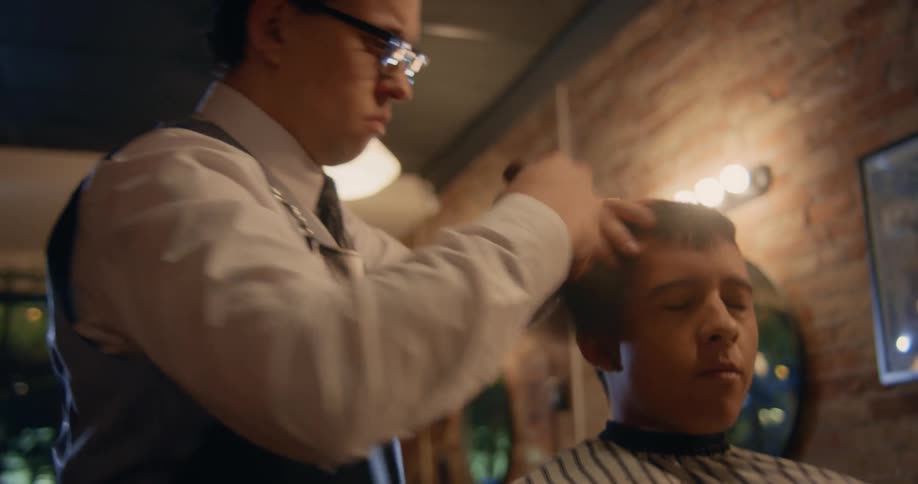 Man seated in a barber shop with the barber brushing his hair the man is shown in a relaxed position with his eyes closed while the barber works on his head