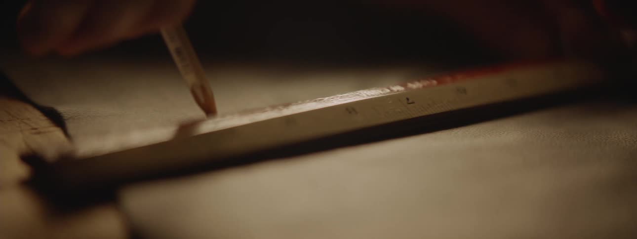 A close up of a ruler on paper as a person marks with a pencil along the ruler