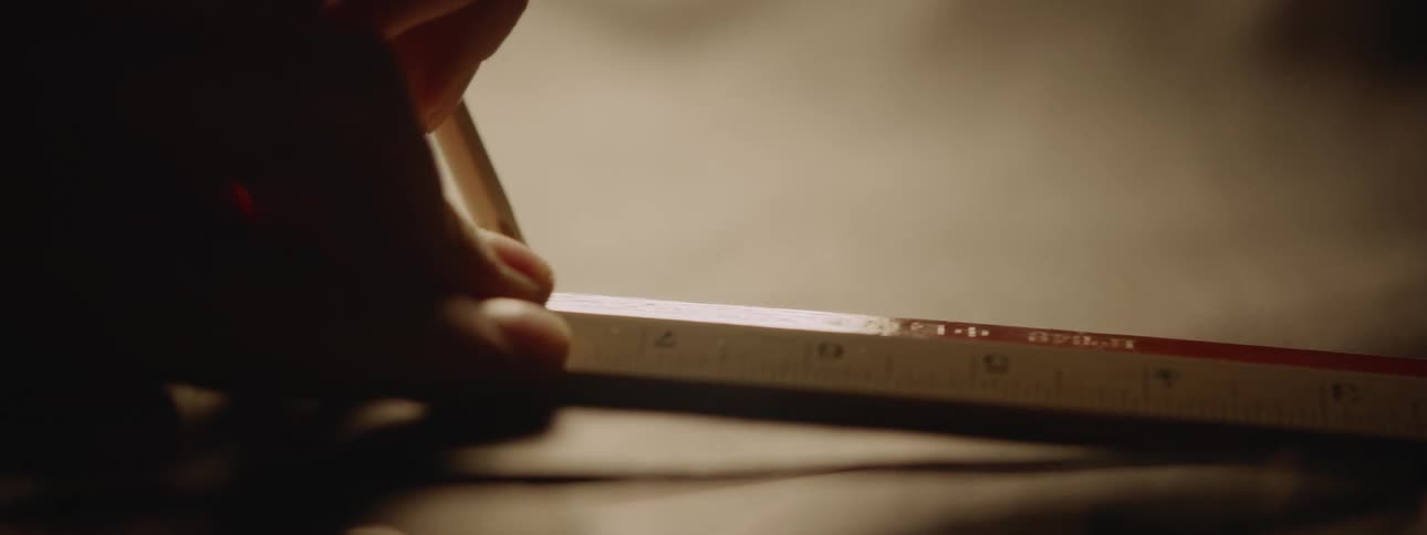 A hand holding a pencil and a ruler actively engaged in measuring something