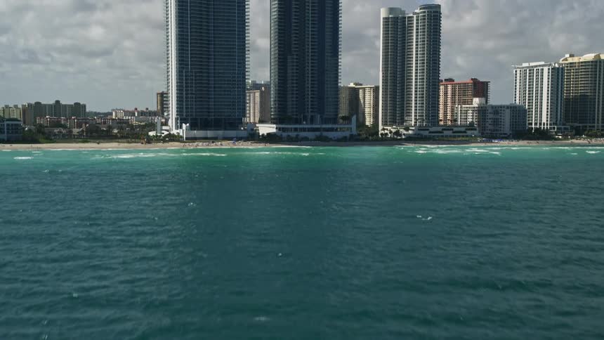Aerial footage capturing the Jade Ocean and Jade Beach condominiums surrounded by a bustling metropolis at Sunny Isles Beach Florida with waves crashing onto the shoreline