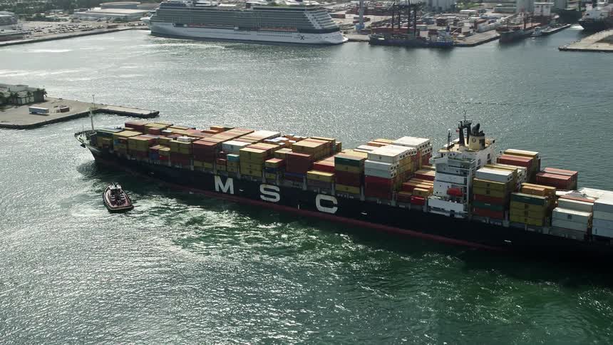Tugboats expertly maneuver a cargo ship into port in Fort Lauderdale Florida viewed from an aerial 