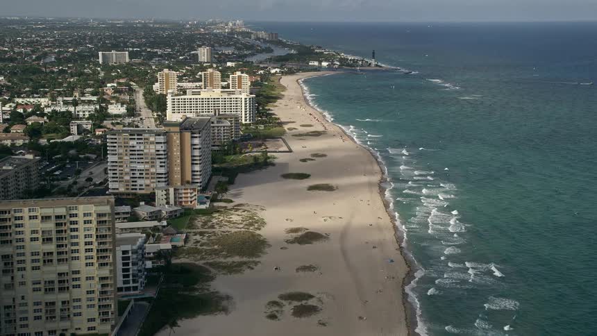 Approaching Hillsboro Inlet Light from aerial view revealing Pompano Beach and condo residences along the shoreline on a partly cloudy day